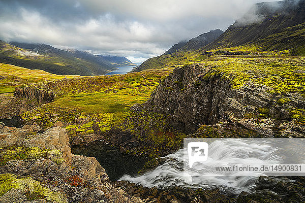 Zerklüftete isländische Landschaft mit leuchtend grüner Tundra und Blick auf die Küstenlinie in der Ferne; Island