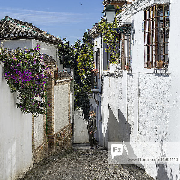 Eine Frau posiert auf einem schmalen Gehweg zwischen den weiß getünchten Häuserwänden; Granada  Spanien