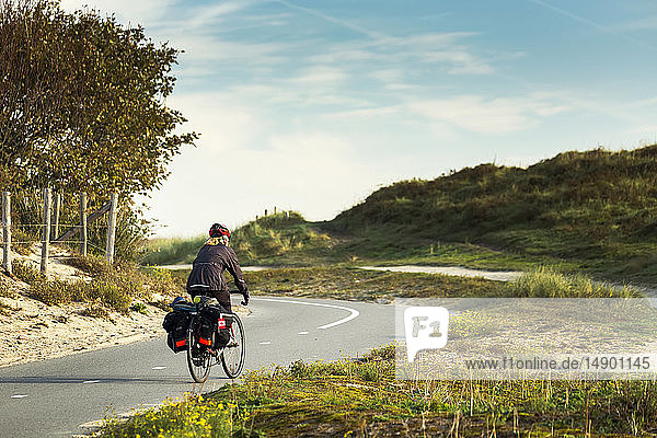 Radfahrerin auf gepflastertem Radweg entlang sanfter Sanddünen und grasbewachsener Hügel  südlich von Zandvoort; Niederlande