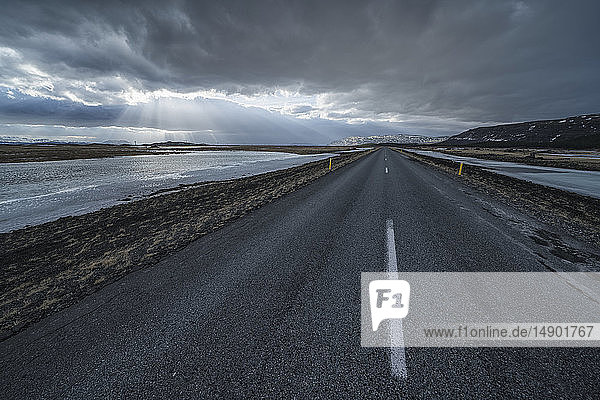 Straße  die in die dramatische Landschaft Islands führt  während die Sonne durch die Wolken scheint und ein schönes Bild abgibt; Island