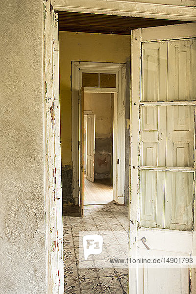 An old worn door open into an empty room with antique ceramic tile floor; Mendoza  Argentina