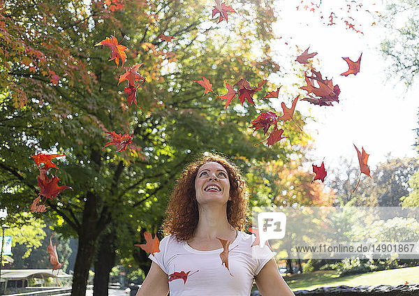 Portrait of a woman with red  curly hair throwing autumn coloured leaves in the air; Burnaby  British Columbia  Canada