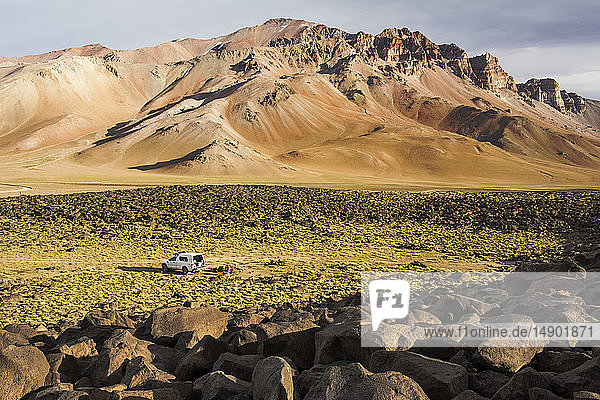 Ein Wohnmobil ist in der Weite eines Hochtals in den Anden geparkt. Die Berge in der Ferne sind vom späten Tageslicht ockerfarben gefärbt; Mendoza  Argentinien