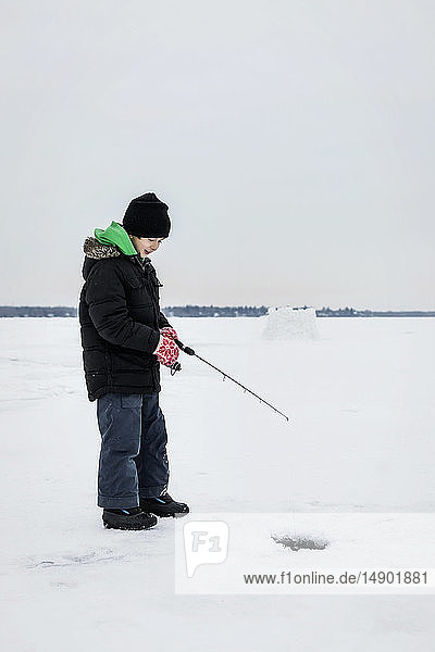 Boy patiently waiting for a bite while ice fishing at Wabamun Lake; Wabamun  Alberta  Canada