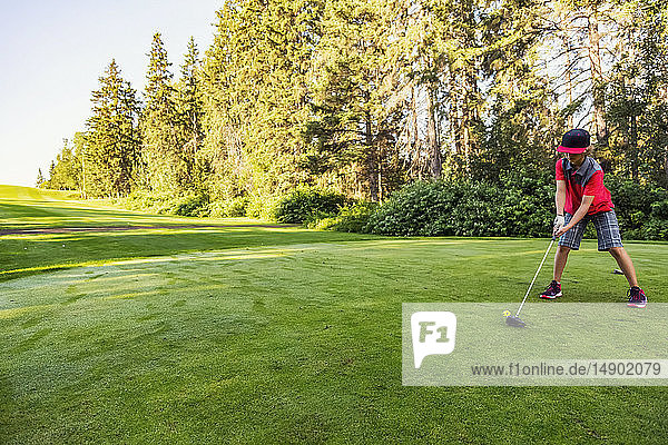 A young boy lines up a shot with a driver using a yellow practise ball on a tee at a golf course during the early morning; Edmonton  Alberta  Canada