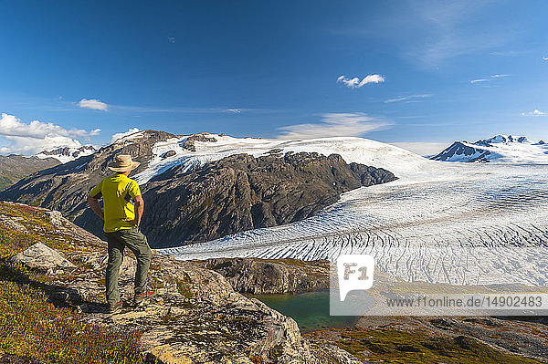 Ein Mann wandert in der Nähe des Harding Icefield Trail mit den Kenai Mountains und einem unbenannten Hängegletscher im Hintergrund  Kenai Fjords National Park  Kenai Peninsula  Süd-Zentral-Alaska; Alaska  Vereinigte Staaten von Amerika
