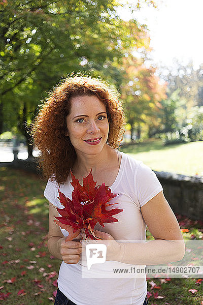 Porträt einer Frau mit rotem  lockigem Haar  die herbstlich gefärbte Blätter hält; Burnaby  British Columbia  Kanada