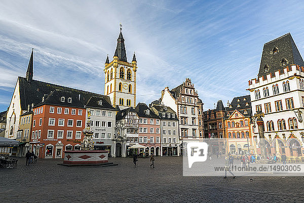 Spaziergänger auf dem mittelalterlichen Marktplatz in einem Dorf mit dekorativem Brunnen  bunten Gebäuden und einem großen Uhrenturm mit blauem Himmel und Wolken; Trier  Deutschland
