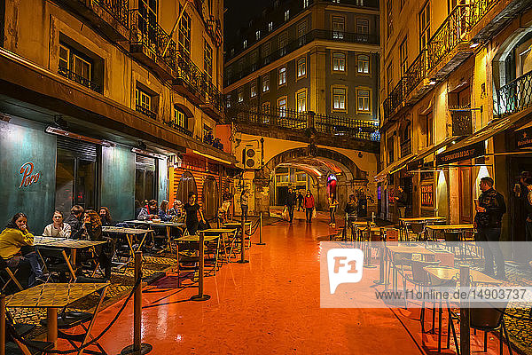 Beleuchtete Sitzplätze im Innenhof bei Nacht zwischen Gebäuden mit Besuchern und Fußgängern; Lissabon  Region Lisboa  Portugal