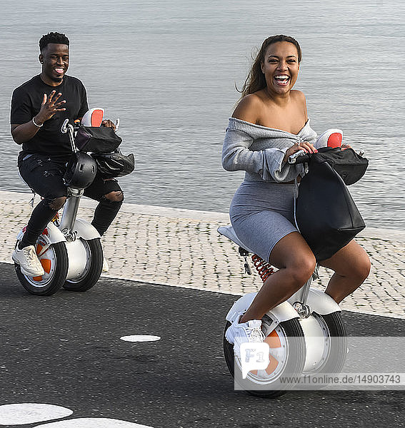 Ein Paar fährt auf Segways einen Weg am Wasser entlang und lächelt in die Kamera; Lissabon  Bezirk Setubal  Portugal