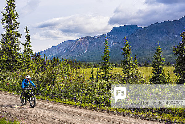 A man fat biking on the Nabesna Road in Wrangell-St. Elias National Park and Preserve on a cloudy summer day in South-central Alaska; Alaska  United States of America