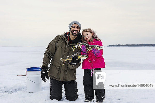 Father and young daughter showing off their catch before releasing it while ice fishing at Lake Wabamun; Wabamun  Alberta  Canada
