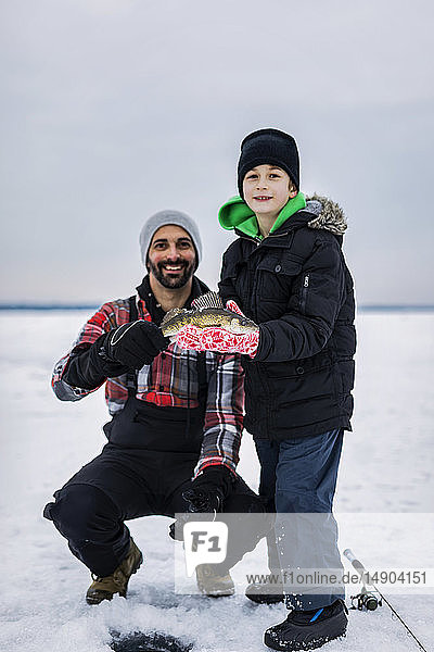 Father and young son showing off their catch of a walleye before releasing it while ice fishing at Lake Wabamun; Wabamun  Alberta  Canada