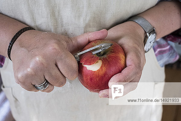 Nahaufnahme einer Person  die einen roten Apfel mit einem Doppelblattschäler schält.