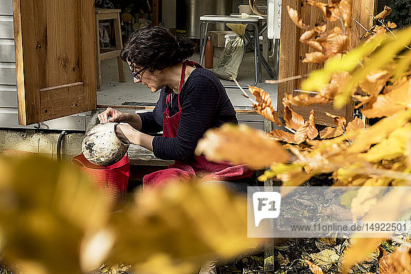 Frau mit roter Schürze sitzt vor ihrer Keramikwerkstatt und hält eine Vase.