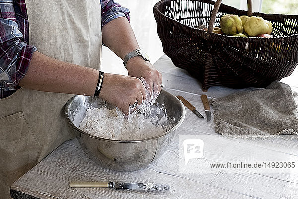 Close up of person wearing apron standing in kitchen  mixing ingredients for a crumble in metal bowl.