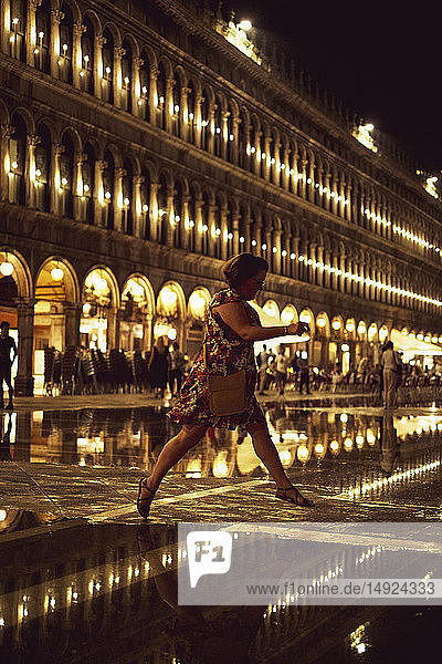 Frau  die nachts über einen beleuchteten Markusplatz in Venedig  Venetien  Italien  hüpft.