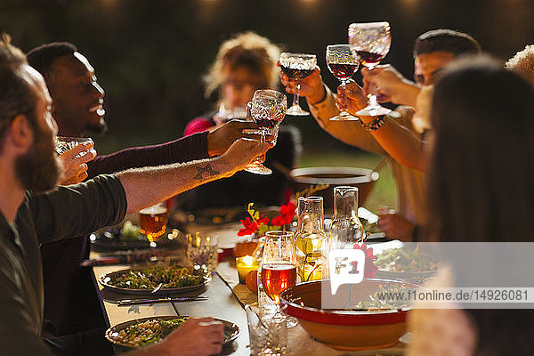 Freunde stoßen mit Weingläsern beim Abendessen auf einer Gartenparty an