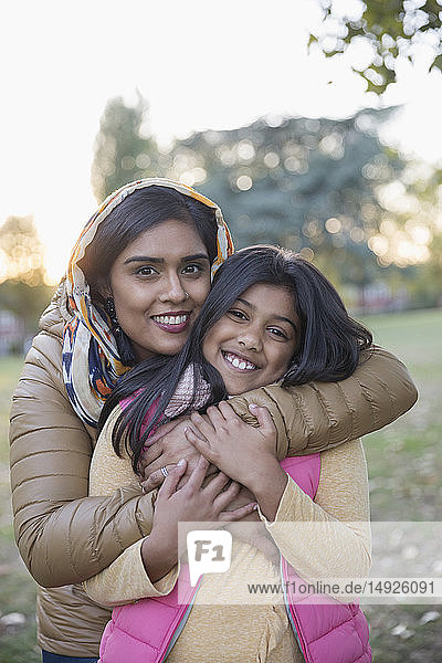 Portrait happy Muslim mother in hijab hugging daughter in park