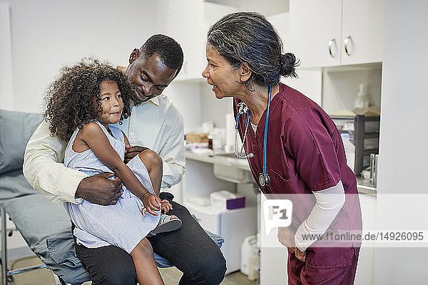 Female pediatrician talking to father and daughter in clinic examination room