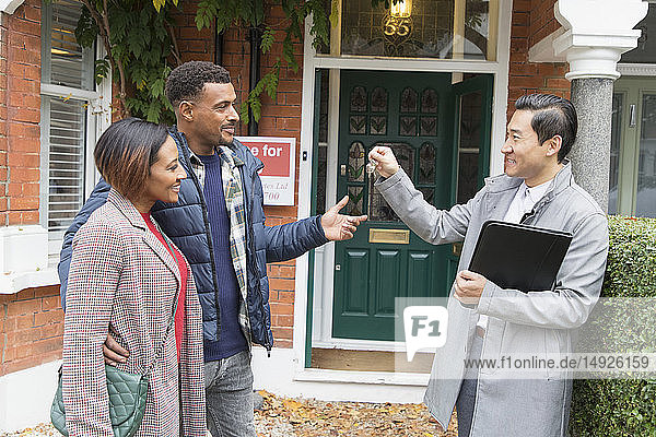 Real estate agent giving house keys to couple outside house for sale