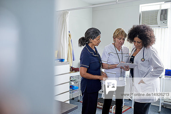 Ärztin und Krankenschwestern benutzen ein digitales Tablet im Untersuchungsraum einer Klinik
