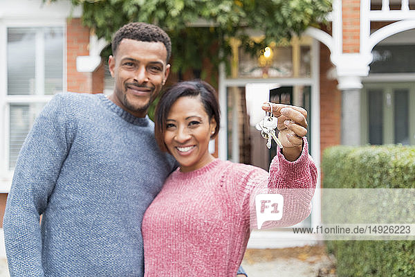 Portrait glückliches Paar mit Hausschlüssel vor neuem Haus