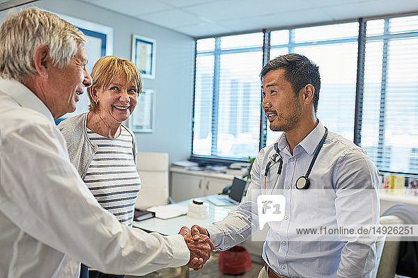 Male doctor shaking hands with senior couple in clinic doctors office
