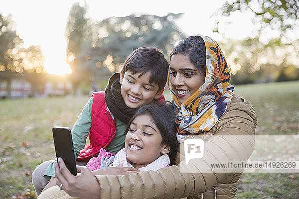 Muslimische Mutter im Hidschab macht Selfie mit Fotohandy im Herbstpark