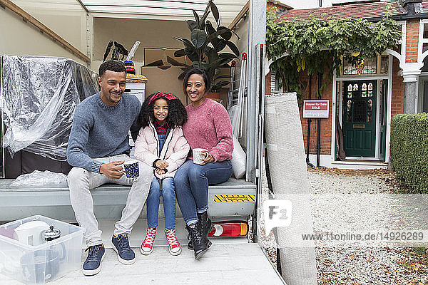 Porträt einer glücklichen Familie beim Teetrinken auf der Ladefläche eines Umzugswagens vor dem neuen Haus