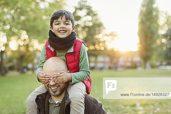 Portrait playful son riding on fathers shoulders in autumn park