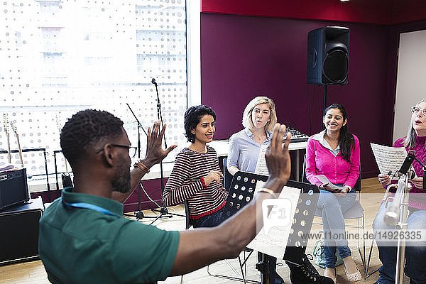 Male conductor leading women singing in music recording studio