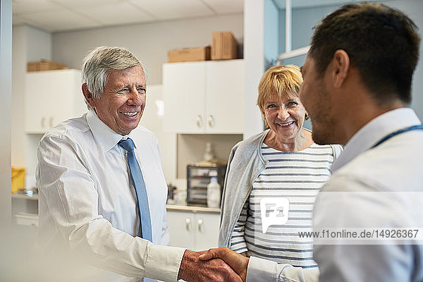 Arzt schüttelt Hände mit älterem Ehepaar im Untersuchungsraum einer Klinik