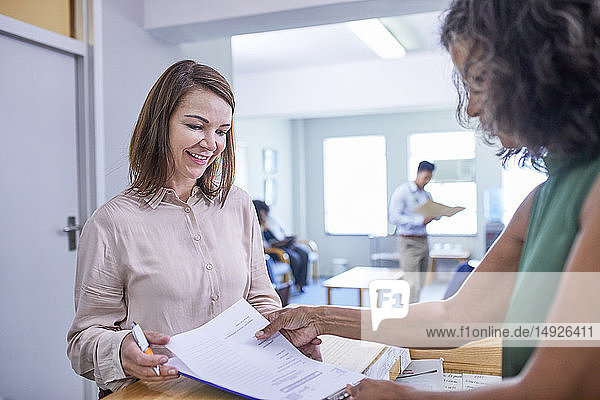 Receptionist helping woman with paperwork at clinic reception