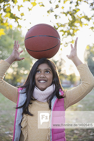 Portrait süßes Mädchen balanciert Basketball auf dem Kopf im Herbst Park
