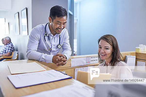 Ein lächelnder Arzt und eine Arzthelferin besprechen die Krankenakte in einer Klinik