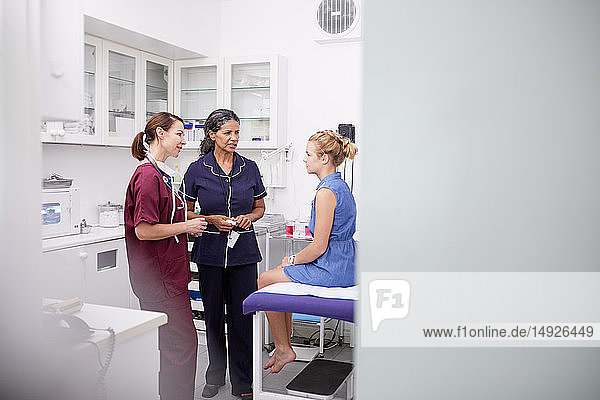 Female doctor and nurse talking to girl patient in clinic examination room