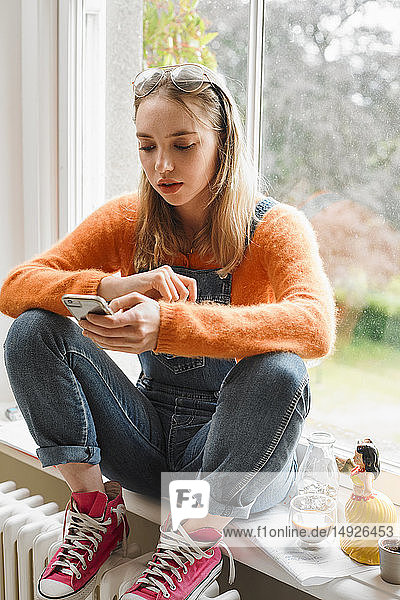 Junge Frau schreibt eine SMS mit einem Smartphone im Fenster