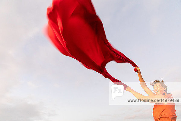 Frau hält rotes  im Wind flatterndes Tuch hoch