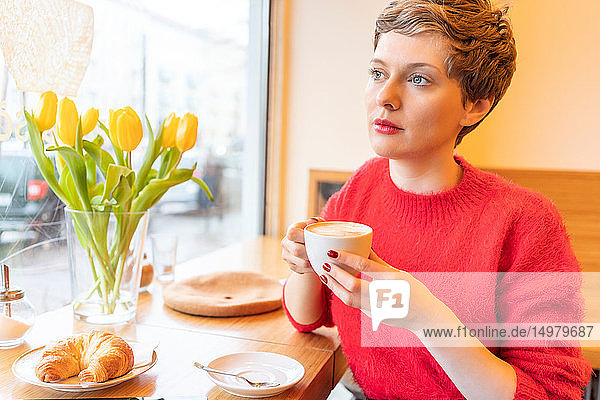 Mittlere erwachsene Frau mit kurzen blonden Haaren  die durch ein Café-Fenster schaut