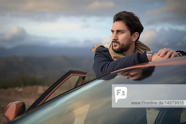 Man resting against car on roadside enjoying view on hilltop