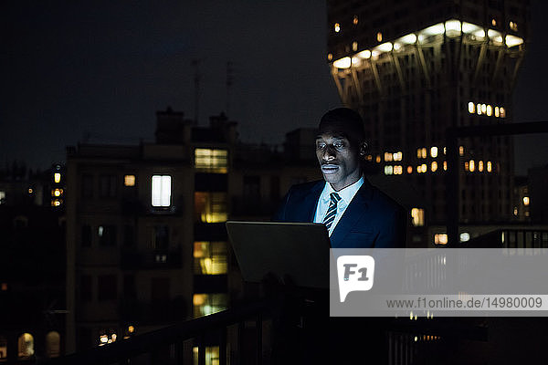 Junger Geschäftsmann benutzt Laptop nachts auf Bürobalkon