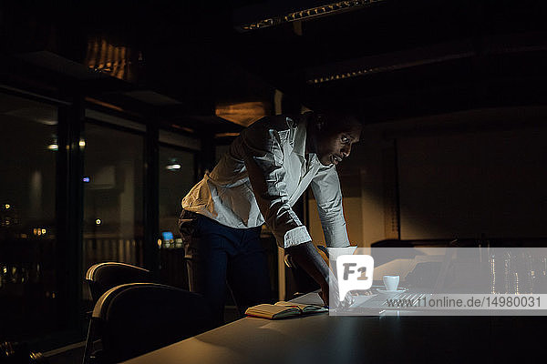 Junger Geschäftsmann  der nachts im Büro sitzt und auf seinen Laptop schaut