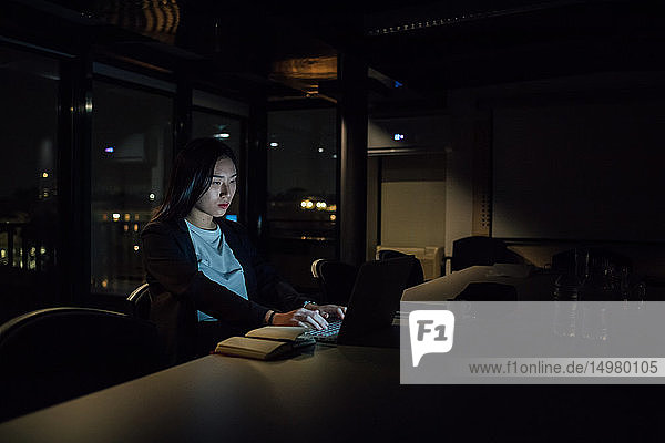 Junge Geschäftsfrau  die nachts im Büro am Laptop tippt
