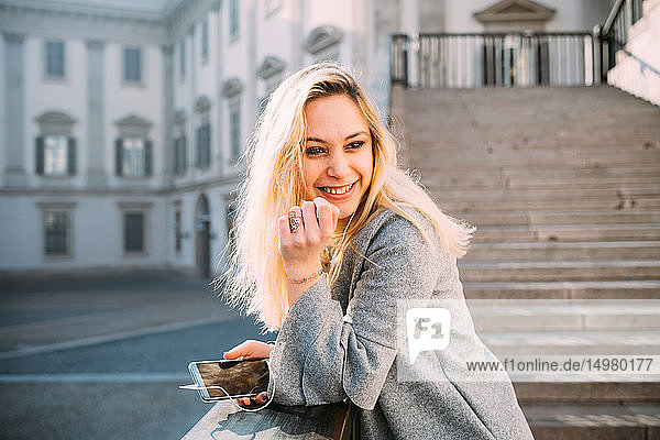 Young woman with long blond hair listening to smartphone music on stairway  Milan  Italy