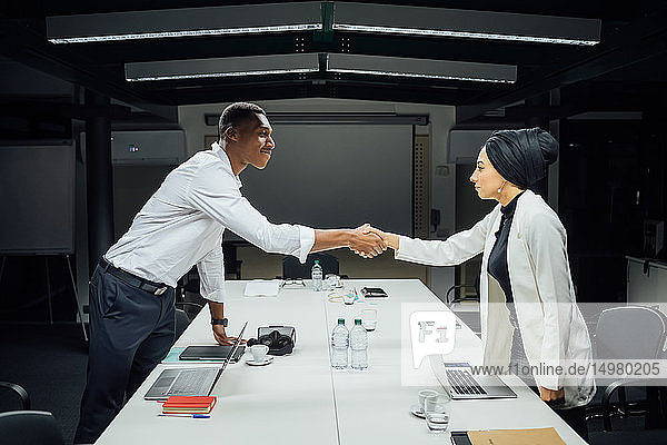 Geschäftsmann und -frau schütteln Hände über Konferenztisch