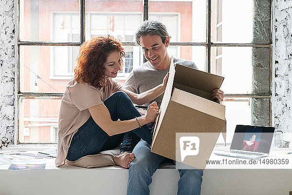 Ehepaar zieht in eine Wohnung im Industriestil sitzt auf Fensterbrettern und schreibt auf Pappkarton