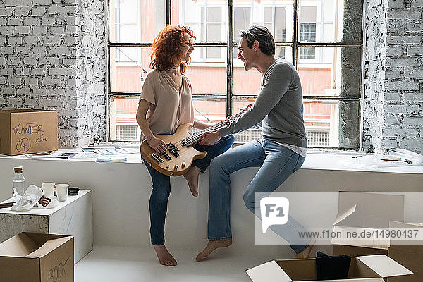 Ehepaar zieht in eine Wohnung im Industriestil sitzt mit Gitarre auf der Fensterbank