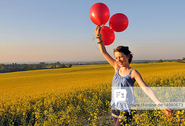 Mädchen mit roten Luftballons auf Rapsfeld  Eastbourne  East Sussex  Vereinigtes Königreich
