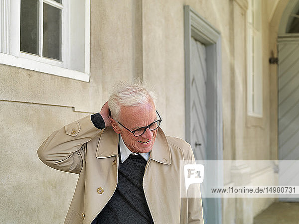 Älterer Mann im Regenmantel  der sich am Kopf kratzt  Kopenhagen  Hovedstaden  Dänemark
